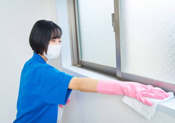 A woman in work clothes and mask wiping the room